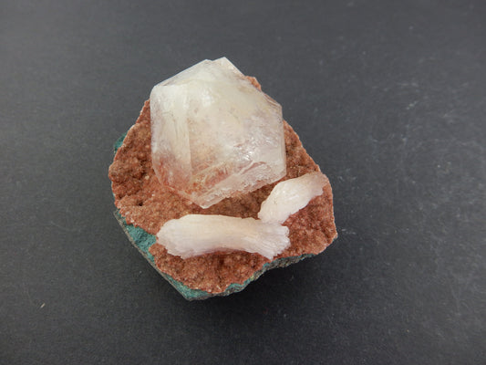 Single gemmy Apophyllite point next to twin Heulandites on a bed of red stilbite?+calcite vug in volcanic matrix