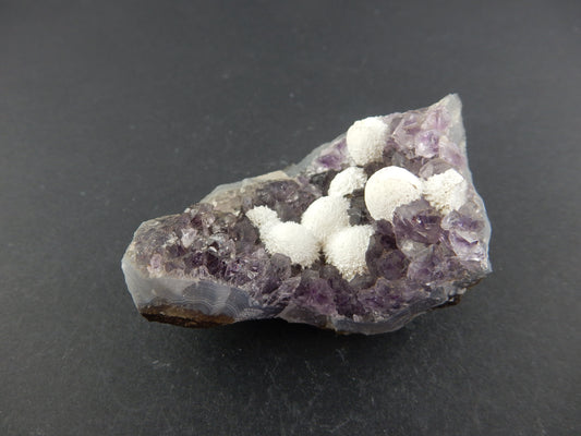 White "snowballs" of Okenite scattered in a cave of purple amethyst